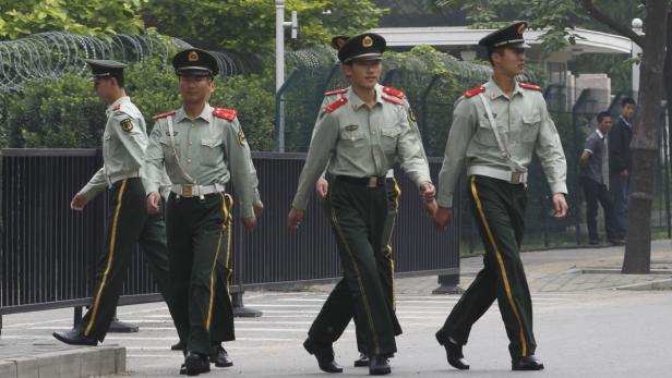 Vier chinesische Soldaten marschieren in Uniform die Straße entlang.