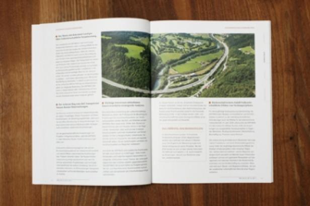 Asfinag/Nachhaltigkeitsbericht/identum Eine geöffnete Zeitschrift zeigt ein Luftbild einer Autobahn durch eine grüne Landschaft.