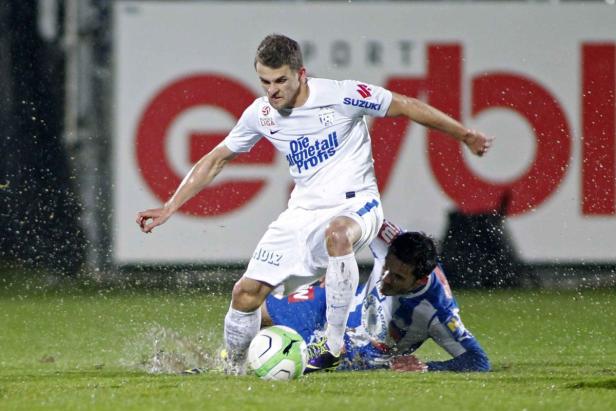 Ein Fußballspieler in Weiß dribbelt den Ball, während ein Gegenspieler zu Boden geht.