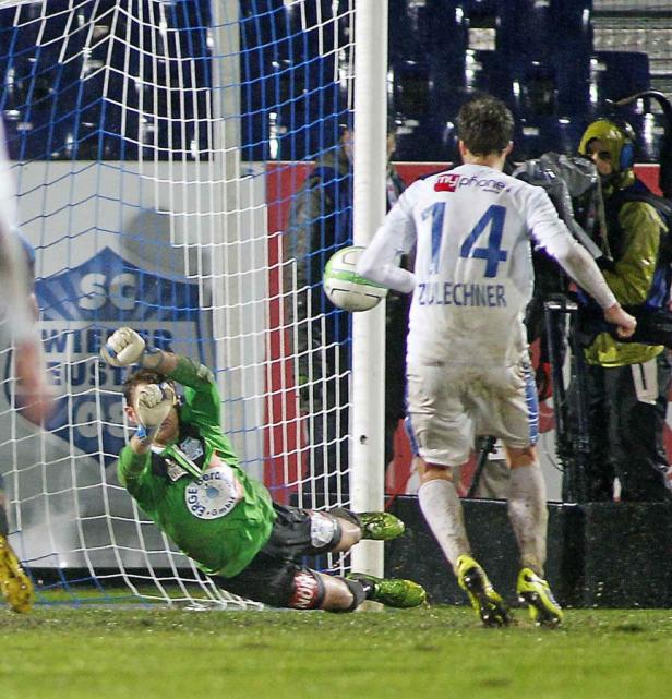 Ein Fußballspieler schießt aufs Tor, während der Torwart versucht, den Ball abzuwehren.