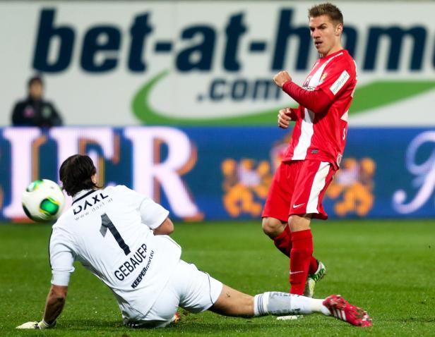 Ein Fußballspieler in Rot schießt den Ball, während ein Torwart in Weiß sich streckt.