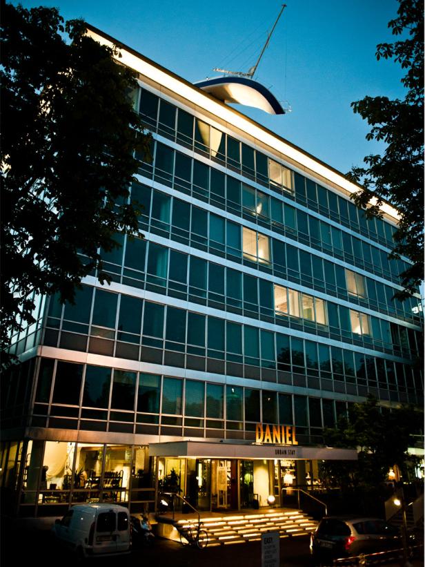 Das Hotel Daniel Urban Stay mit einem Bootsmodell auf dem Dach bei Dämmerung.