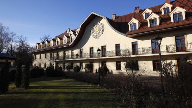 Ein großes, helles Gebäude mit einem Zifferblatt unter dem Dach und einem gepflegten Garten.