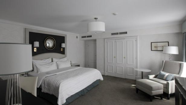 Ein helles Hotelzimmer mit einem großen Bett und einem Sessel mit Fußhocker.