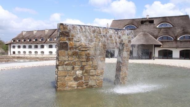 Ein Wasserfall vor dem „Hotel Remes Sport & Spa“ mit einem Gebäude im Hintergrund.