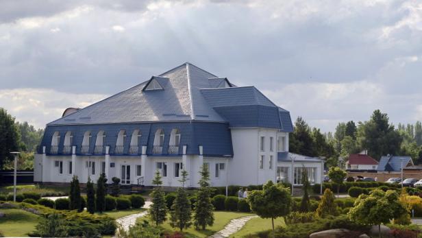 Ein großes, weißes Gebäude mit blauem Dach inmitten einer gepflegten Gartenanlage.