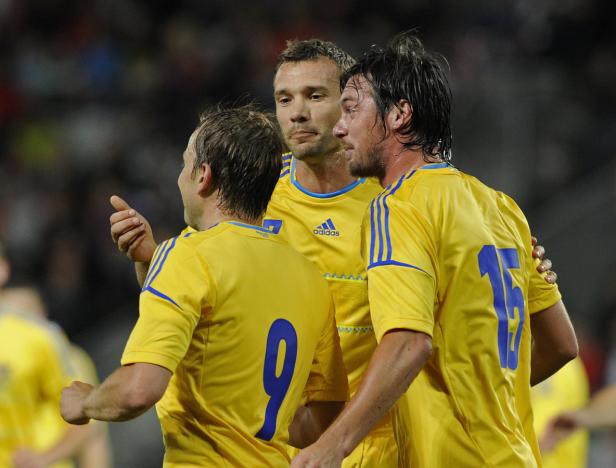 Drei Fußballspieler in gelben Trikots stehen zusammen auf dem Spielfeld.
