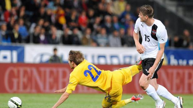 Ein Fußballspieler in Gelb grätscht nach dem Ball, während ein Spieler in Weiß zusieht.