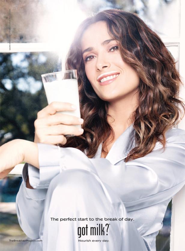 Salma Hayek mit einem Milchbart und einem Glas Milch in der Hand.