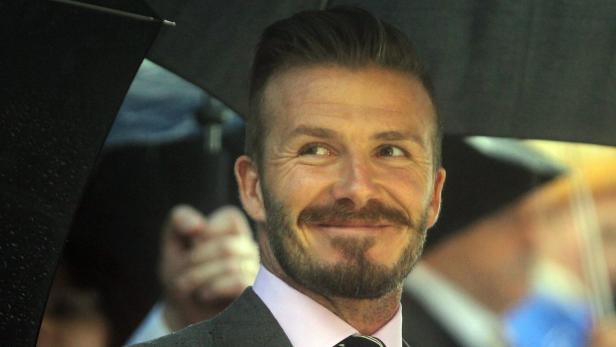 David Beckham lächelt unter einem Regenschirm.