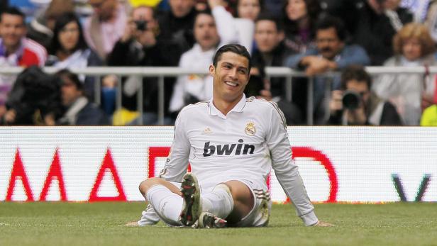 Cristiano Ronaldo sitzt lächelnd auf dem Rasen.