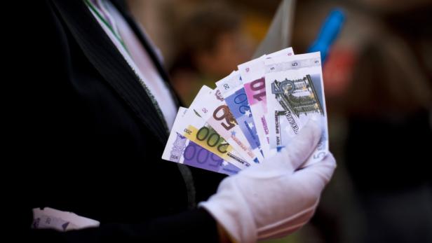 Eine Hand mit weißen Handschuhen hält einen Fächer aus Euro-Spielgeld.