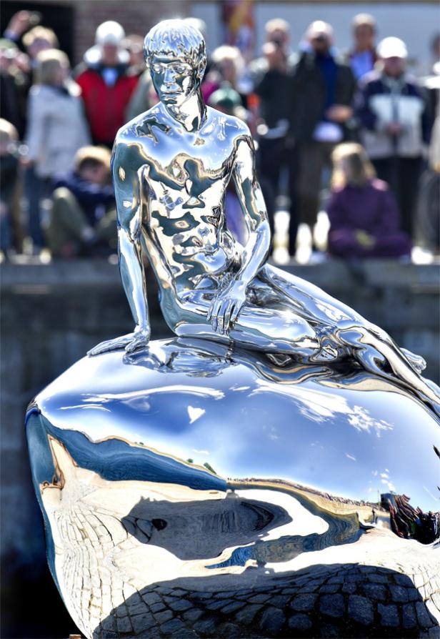 Eine glänzende, silberne Statue der kleinen Meerjungfrau sitzt auf einem Felsen.