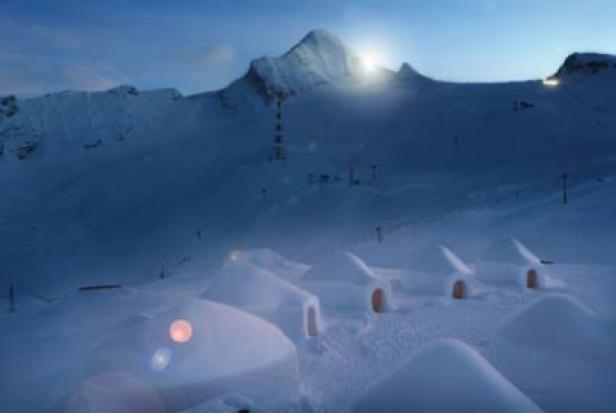 Mehrere Iglus stehen in einer verschneiten Berglandschaft.