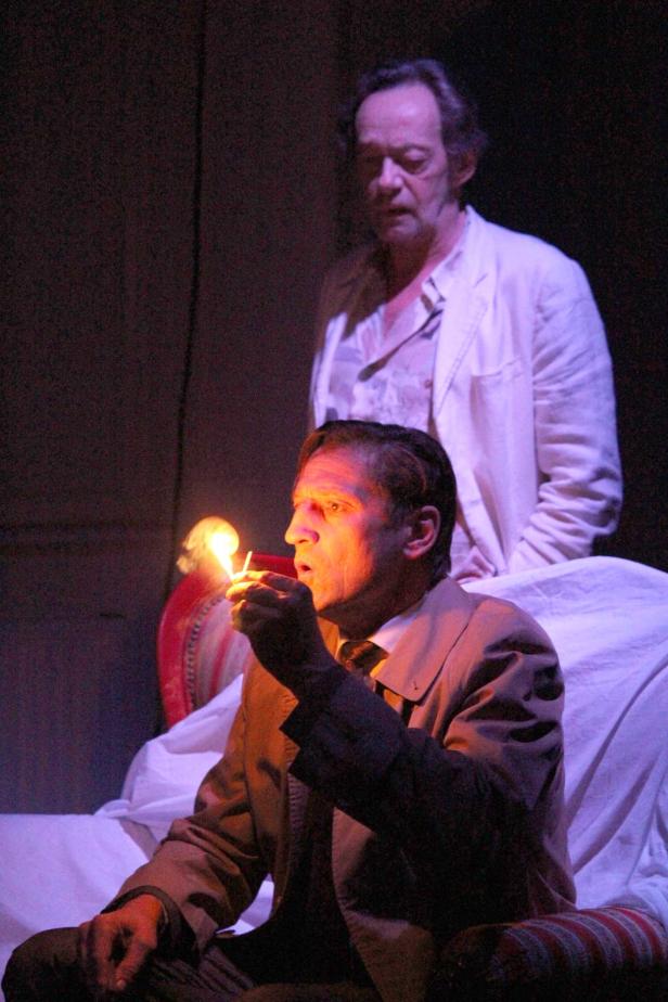 Ein Mann zündet sich eine Zigarette mit einem Streichholz an, während ein anderer Mann im Hintergrund steht.