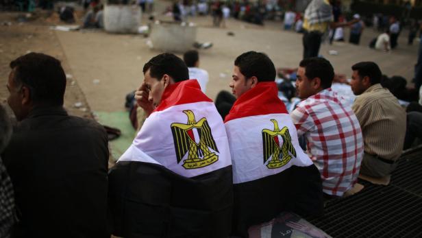 Zwei Männer mit ägyptischen Flaggen sitzen in einer Menschenmenge.