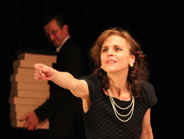 Eine Frau hält einen Schlüssel hoch, während ein Mann im Hintergrund eine Stapel Kartons trägt.