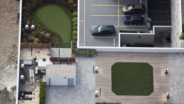 Ein Dachgarten mit Golfrasen, Terrasse und Parkplatz von oben gesehen.