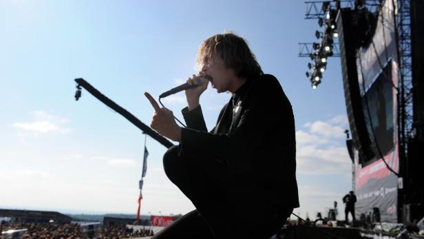 Ein Sänger kniet auf der Bühne und singt in ein Mikrofon.