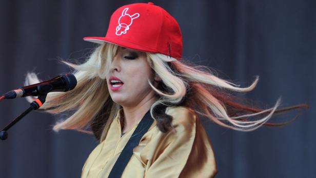 Eine Sängerin mit roter Kappe und blonden Haaren singt in ein Mikrofon.