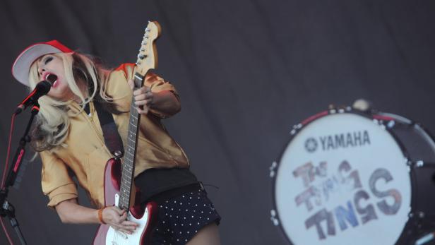 Eine Sängerin der Band The Ting Tings spielt Gitarre und singt in ein Mikrofon.