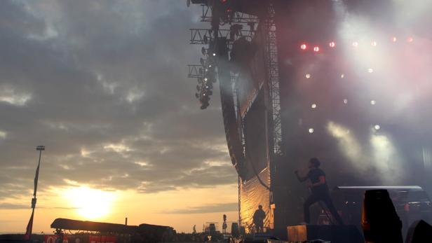 Ein Sänger steht auf einer Bühne während eines Konzerts bei Sonnenuntergang.