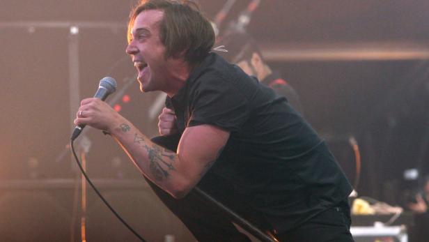 Ein Sänger mit Tätowierungen singt mit einem Mikrofon auf der Bühne.