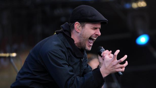 Ein Sänger mit Schirmmütze singt mit Mikrofon auf einer Bühne.