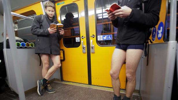 Zwei Männer in Unterhosen lesen in einem gelben U-Bahn-Waggon Bücher.