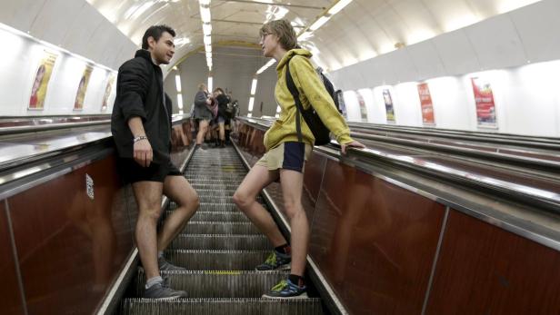 Zwei Männer ohne Hosen stehen auf einer Rolltreppe in einer U-Bahn-Station.