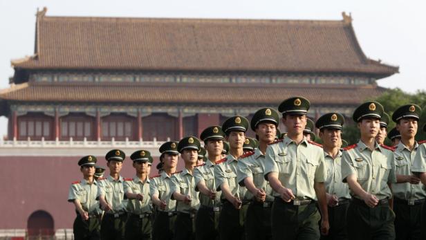 Eine Reihe chinesischer Soldaten marschiert vor einem traditionellen chinesischen Gebäude.