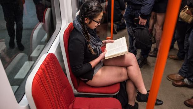 Eine Frau liest in der U-Bahn ein Buch, während andere Fahrgäste um sie herumstehen, die keine Hosen tragen.