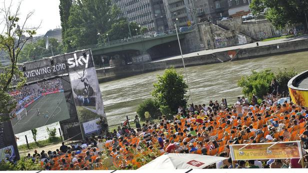 Viele Menschen sitzen vor einer großen Leinwand und schauen ein Fußballspiel.