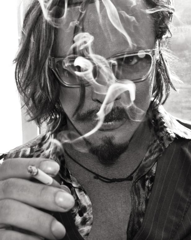 Ein Mann mit Brille und Bart raucht eine Zigarette, Rauch umgibt sein Gesicht.