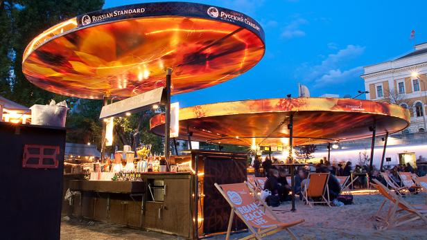 Eine belebte Strandbar mit Liegestühlen und dem Logo von Russian Standard Wodka.