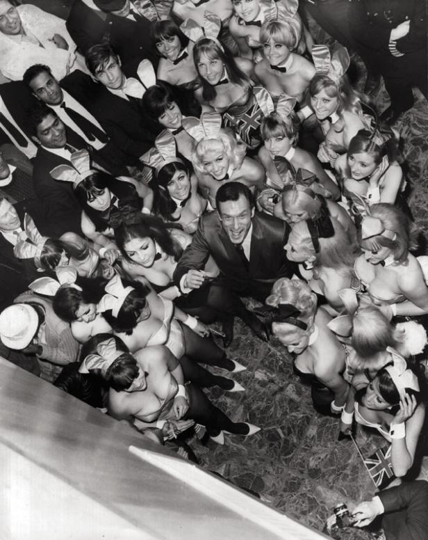 Hugh Hefner umgeben von Playboy Bunnies in einem Schwarzweißfoto.