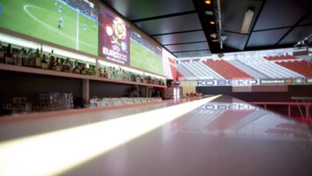 In einer Bar wird ein Fußballspiel auf einer großen Leinwand gezeigt.