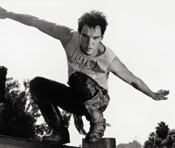 Ein junger Mann in Stiefeln und T-Shirt balanciert auf einem Holzpfosten.