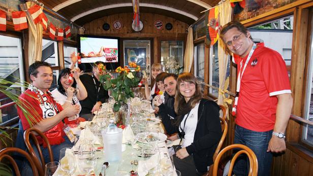 Eine Gruppe von Menschen feiert in einem dekorierten Waggon mit österreichischen Flaggen.