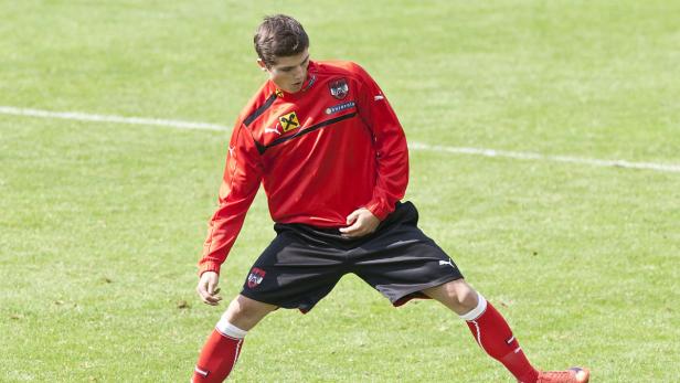 Ein österreichischer Fußballspieler dehnt sich auf einem grünen Rasen.