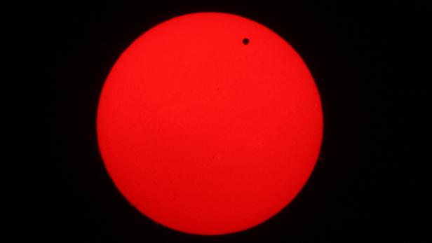 Die Venus ist als schwarzer Punkt vor der roten Sonnenscheibe zu sehen.