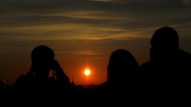 Silhouetten von Menschen beobachten den Sonnenuntergang über der Stadt.