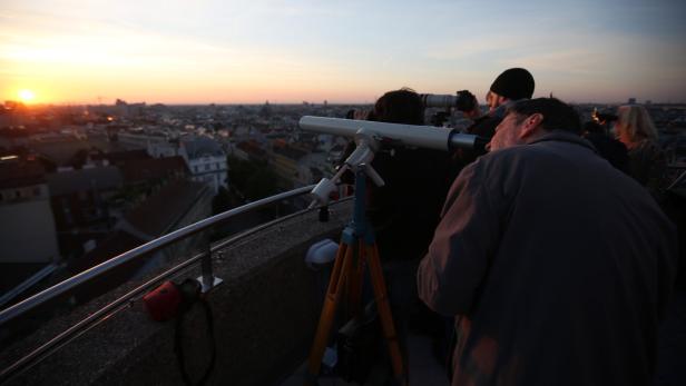 Menschen beobachten den Sonnenuntergang über der Stadt mit Teleskopen und Kameras.