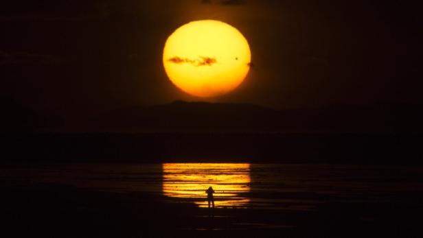 Eine Person steht am Ufer, während die Sonne im Meer untergeht.