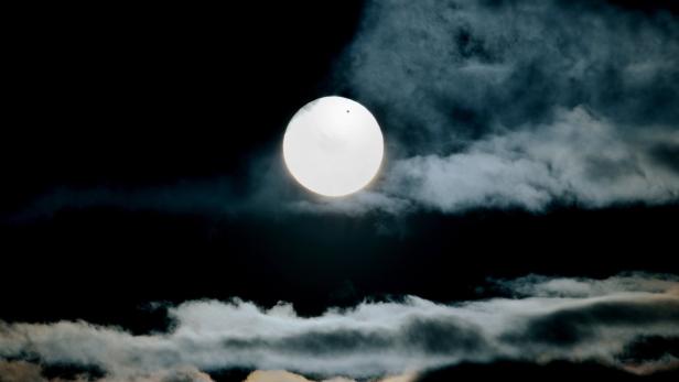 Die helle Sonne scheint durch die Wolken am dunklen Himmel.