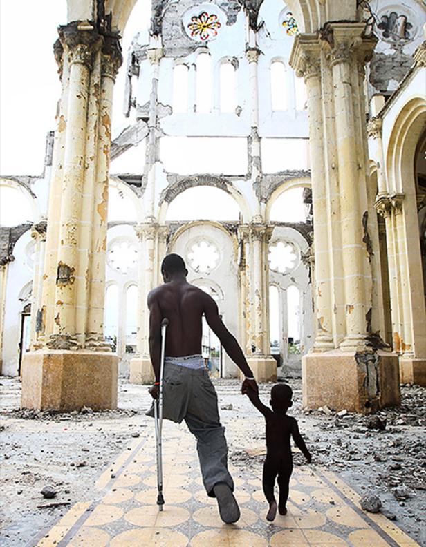 Ein Mann mit Krücke geht mit einem Kind durch die Ruinen einer zerstörten Kirche.