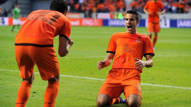 Ein jubelnder Fußballspieler im orangefarbenen Trikot kniet auf dem Rasen.