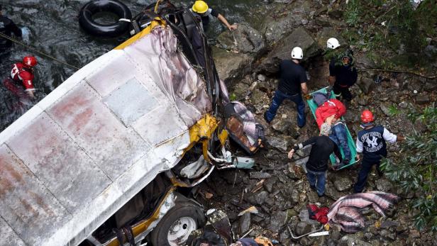 Ein verunglückter Bus liegt in einem Flussbett, während Rettungskräfte Verletzte bergen.