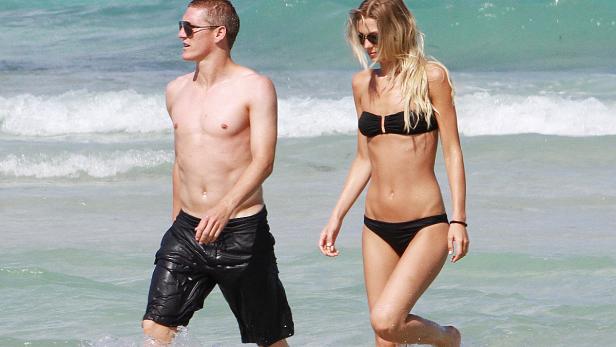 Ein Mann ohne Hemd und eine Frau im Bikini gehen am Strand entlang.