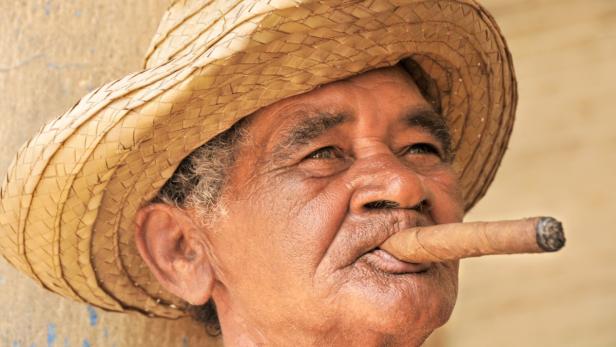 Ein älterer Mann mit Strohhut raucht eine Zigarre.